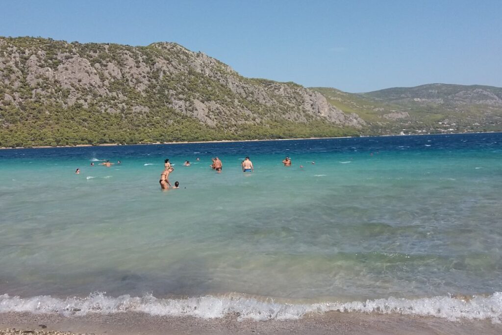 Things to Do in Loutraki Greece. The turquoise Vouliagmeni lake with swimmers and mountain view around