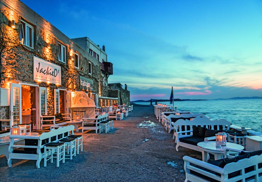 Sea side bar Jackie-o with many tables and chairs and a blue sky in the evening.
In Mykonos Island.
