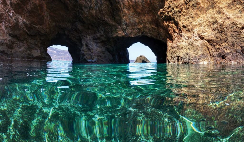 Tragonisi Caves with green water in Mykonos Island.