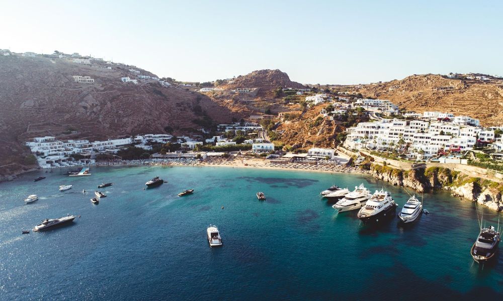 Some yachts in the sea and in the background whitewashed houses. 
Psarou Beach on Mykonos Island