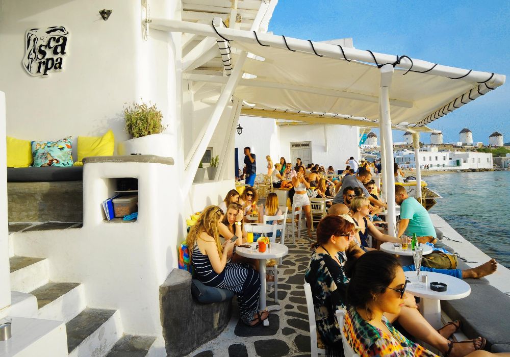 Scarpa bar on Mykonos island in front of sea with many people sitting.