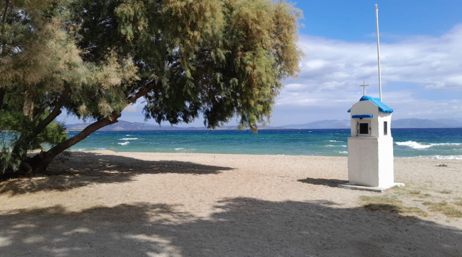 Small seaside chapel under a tree on Marathon Beach with turquoise waters in the background.