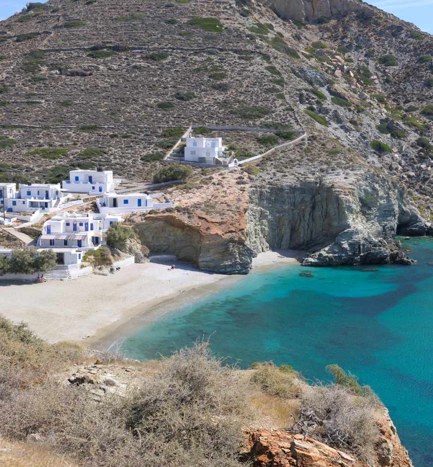 Agali Beach in Folegandros, Greece, with turquoise water, a sandy shore, whitewashed houses and steep rocky cliffs.