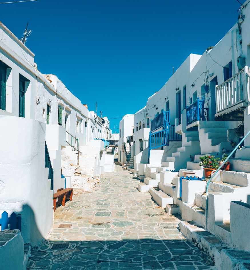 Traditional whitewashed houses with blue doors and balconies along a stone-paved street in Chora, Folegandros, Greece.