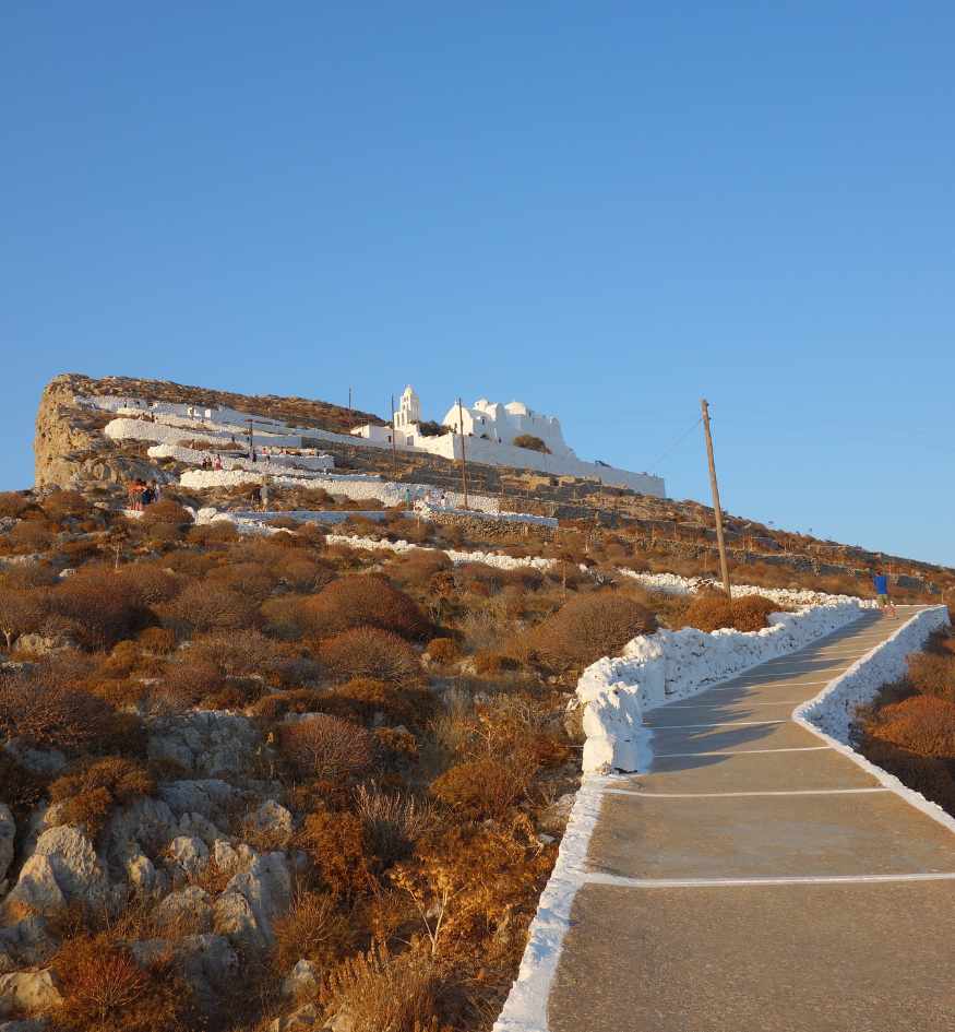 Winding paved path leading uphill through the dry landscape to the Church of Panagia in Folegandros, Greece.