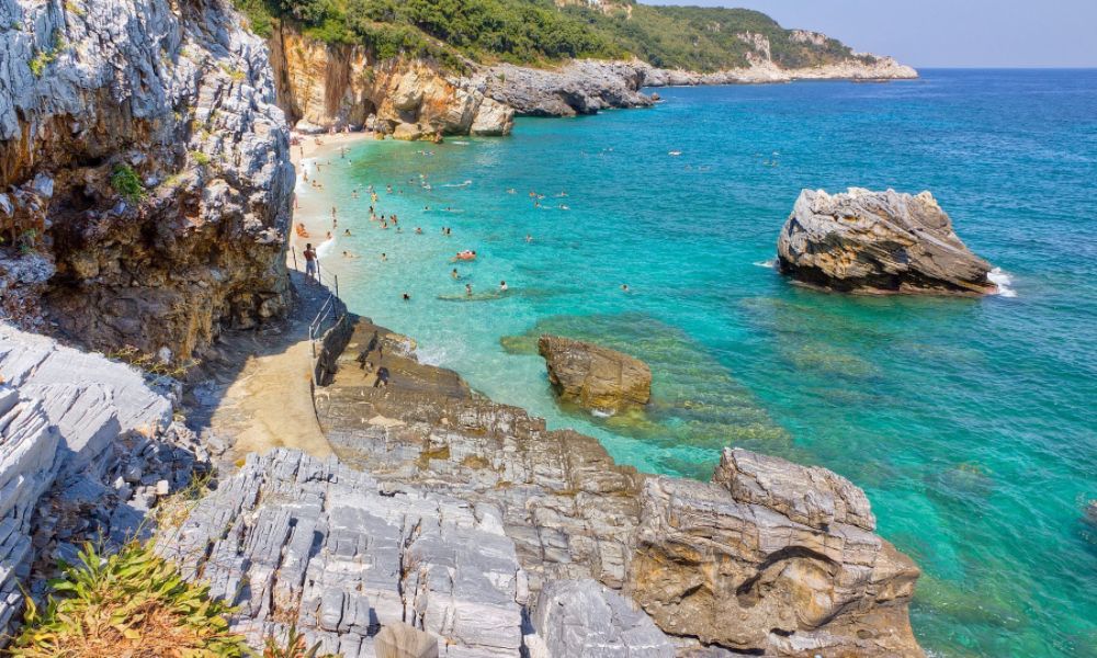 A rocky beach with many people swimming in a sunny day in Mylopotamos beach in Pelion Greece.