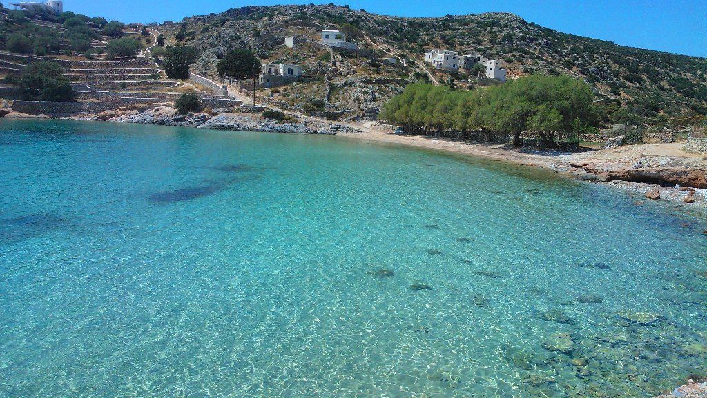 Blue green water and some whitewashed houses in Mersini Beach in Mykonos Island.