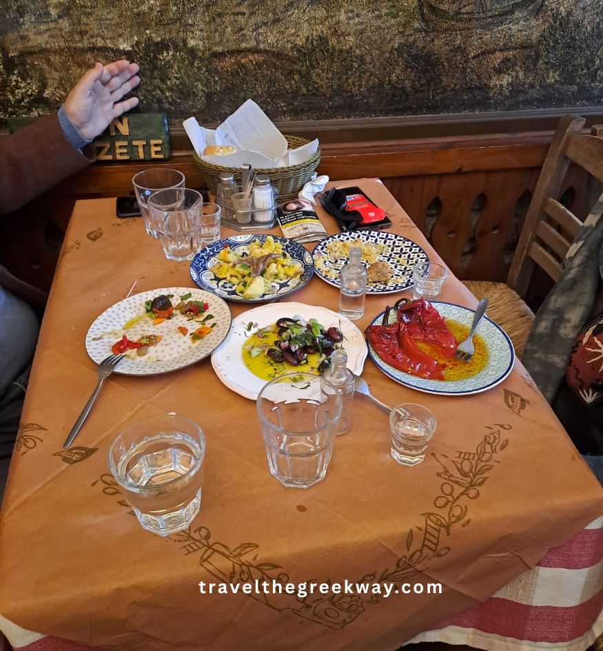 Several small plates of Greek meze, including roasted peppers and olives, on a brown paper-covered table at Tavern Theofilos in Makrinitsa, Pelion, Greece.