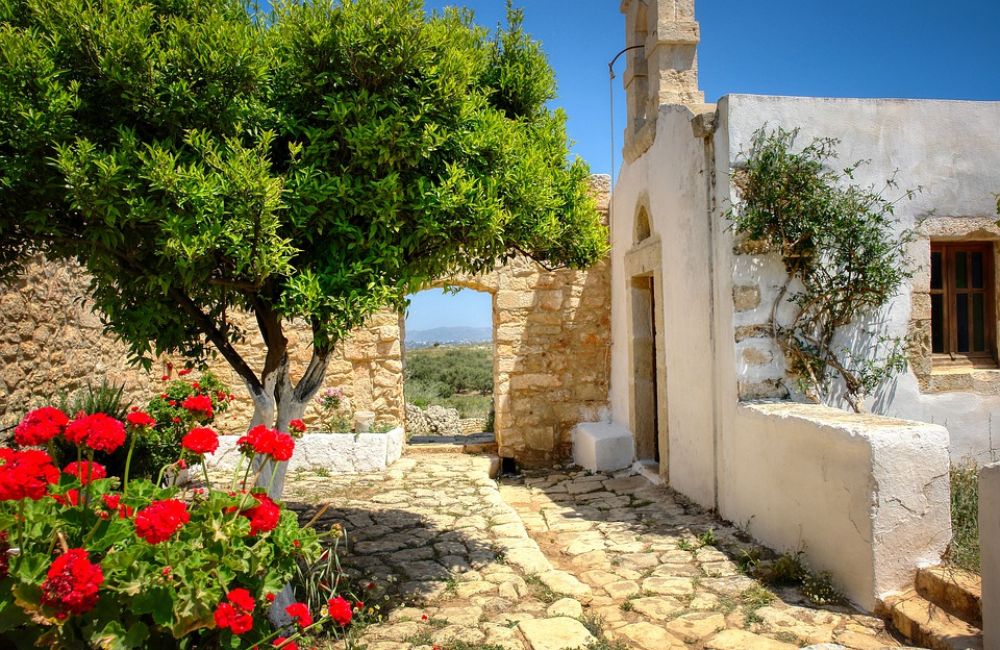 An old Greek Church in a Cretan Village with a tree and red flowers in Chania Crete Greece.