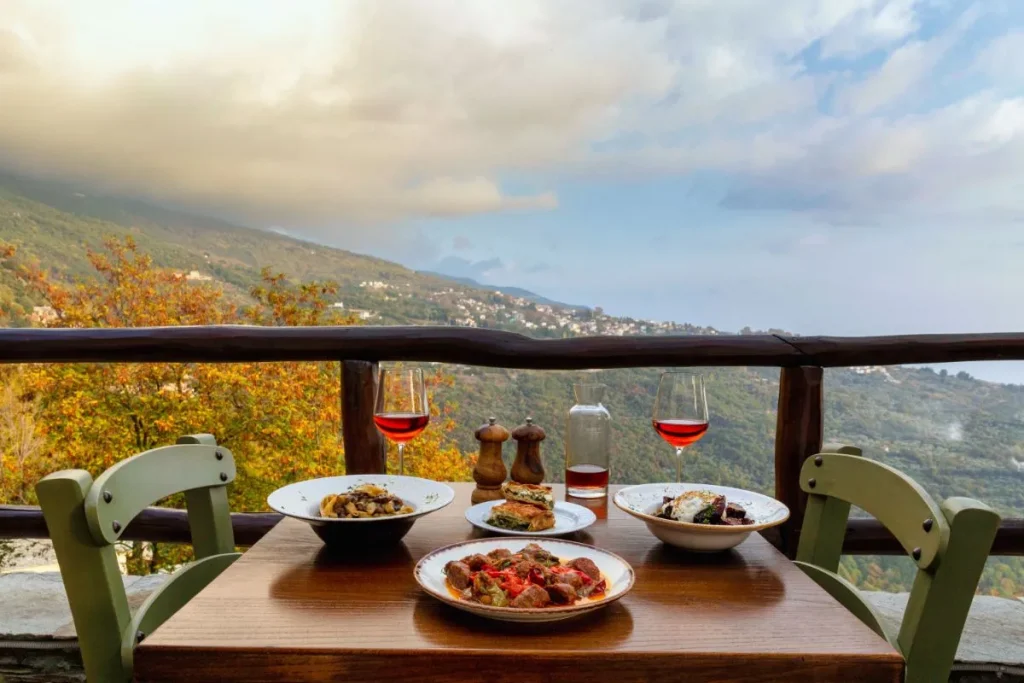 A restaurant called Kardamo with food on the table and red wine and a beautiful view in Pelion Greece. 