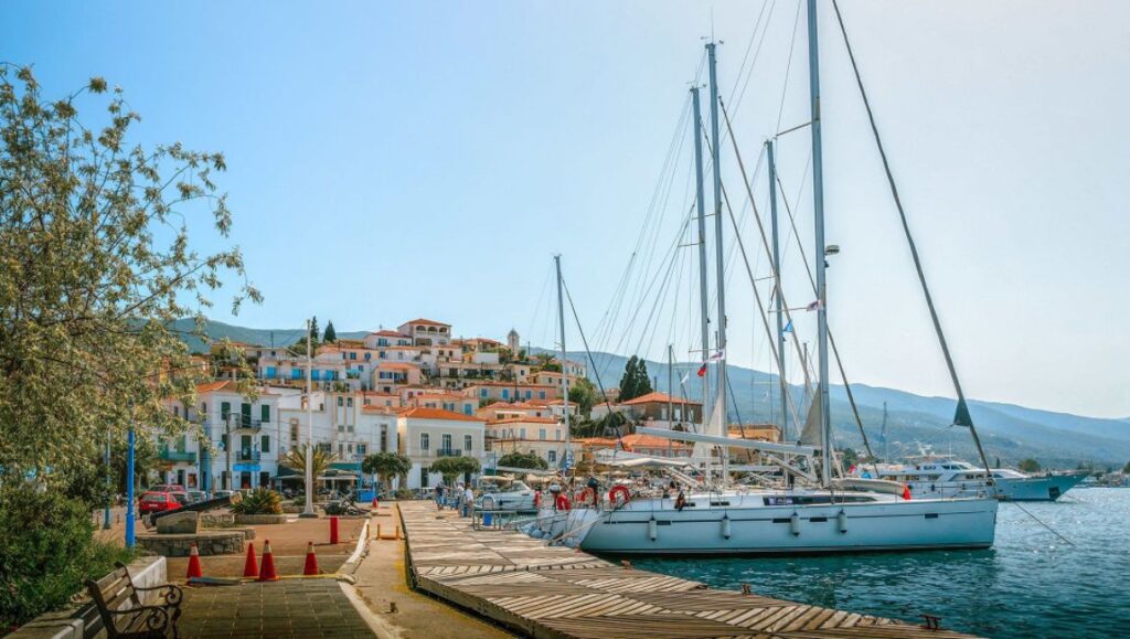 Poros Boulevard, whitewashed houses and a yacht in the sea in Poros Island Greece. 