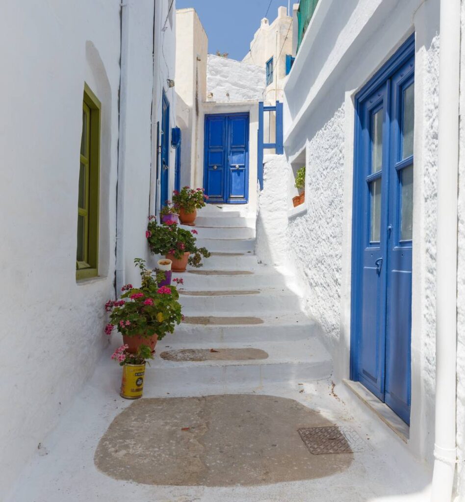 Whitewashed alley with blue doors and flower pots in Chora, Amorgos Greece—beautiful village scenery for any Amorgos travel guide.