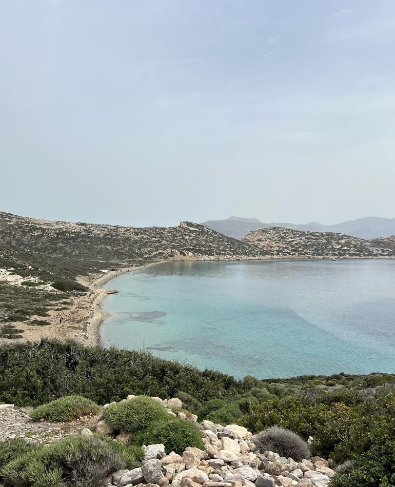 Seaside view of Nikouria islet with stone houses and mountain backdrop in Amorgos.