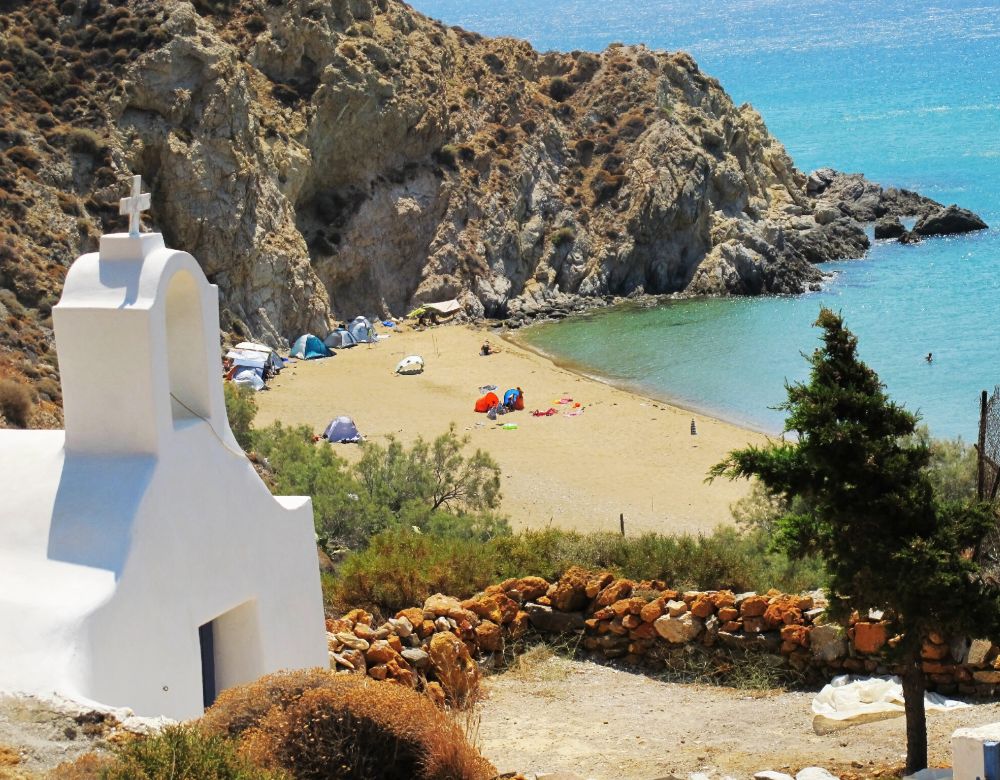 Sandy Agioi Anargyroi Beach with a whitewashed church and many campers 