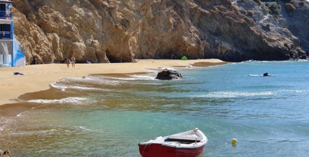 Agios Nikolaos sandy beach and a fishing boat in the sea in Anafi