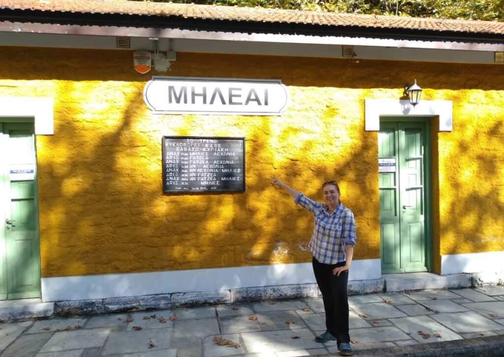 Evgenia in front of a traditional coffee shop called Milee with yellow wall and green door in Pelion Greece.