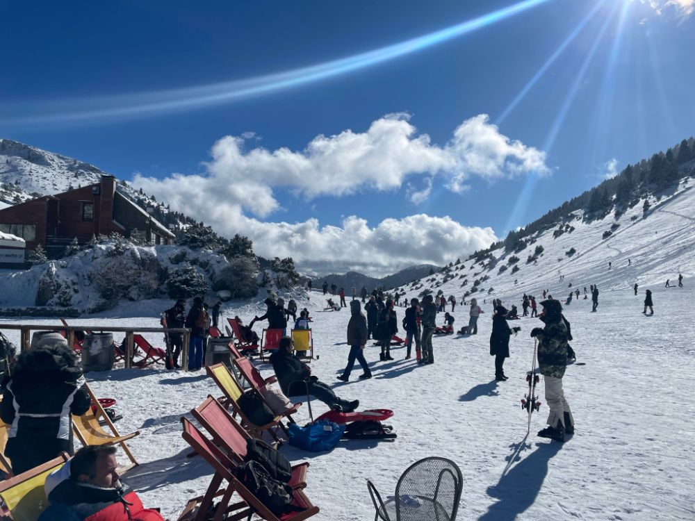 The Menalon ski center with many skiers, people sitting on chairs and a chalet. Ski resorts in Greece.