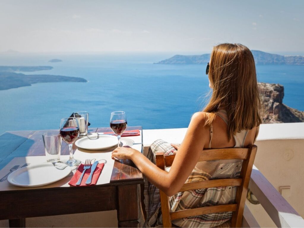 A young woman sitting at a table drinking wine in Santorini