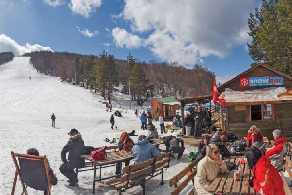 Lailia ski center with chalet, people sitting outside chatting and some skiing