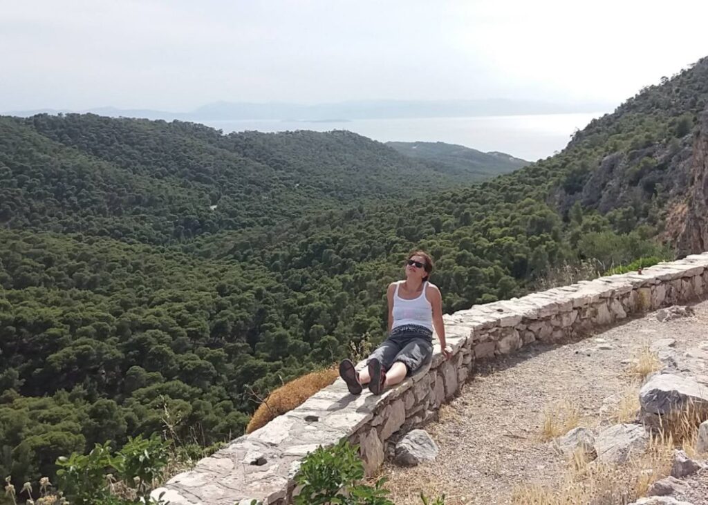 Evgenia resting on a ledge over a Greek forest