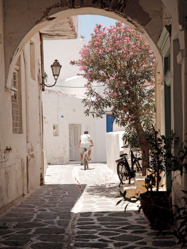 A man biking on a whitewashed cobblestone alley on paros island in Greece. 