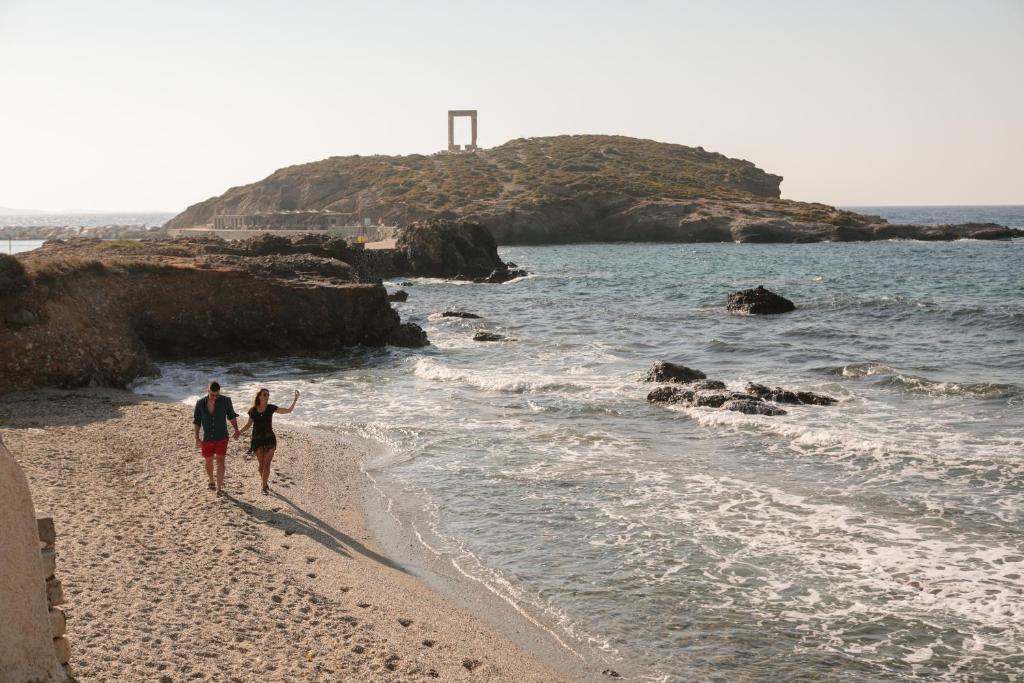 Couple walking on a secluded beach in Naxos with the iconic Portara in the background.