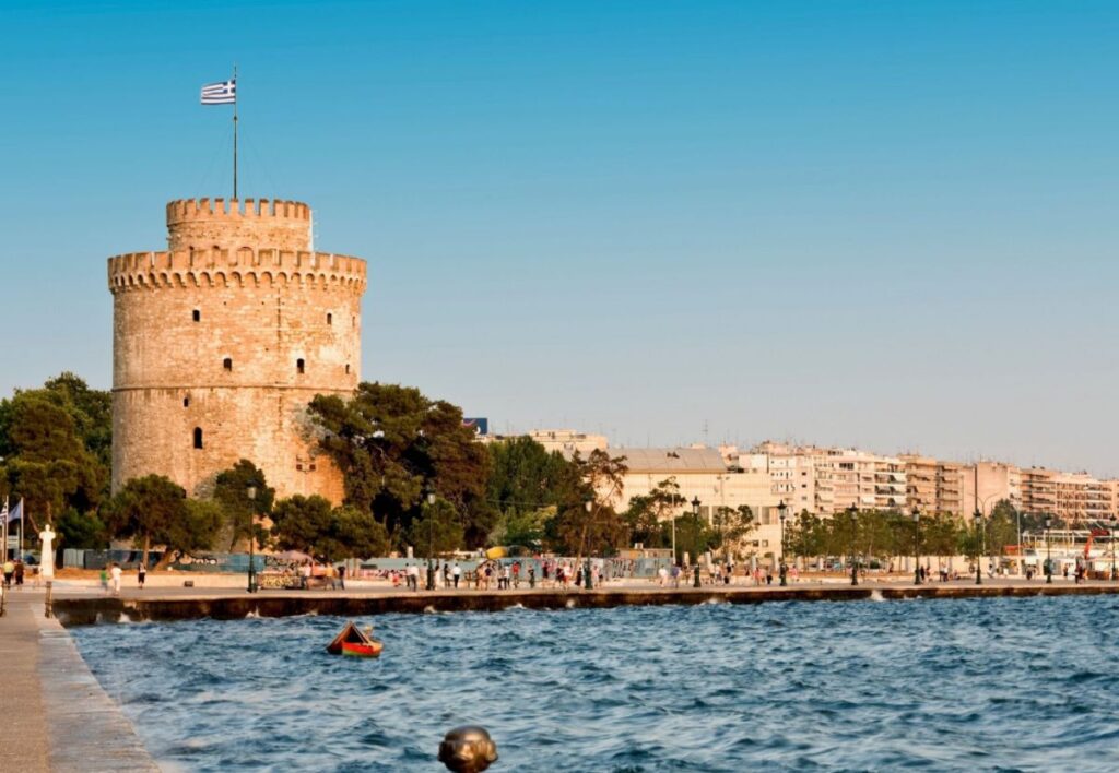 The Best Hotels in Thessaloniki - The Ottoman White Tower srtanding in front of the sea with people walking in front of it