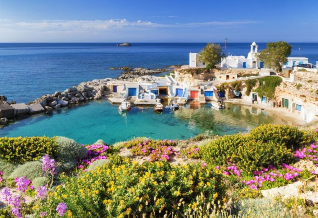 A Small Port Surrounded of Green and Whitewashed Houses with Blue Sky in Milos Greece. 