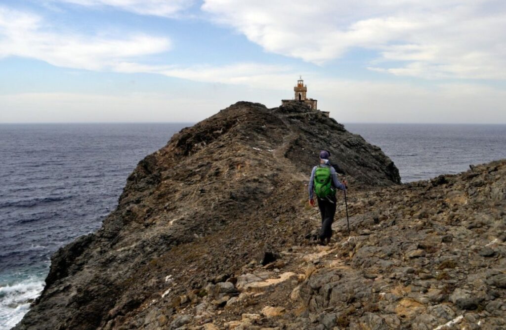 Hiking Cyclades Islands, hiker pproaching a lighthouse on tinos island Greece