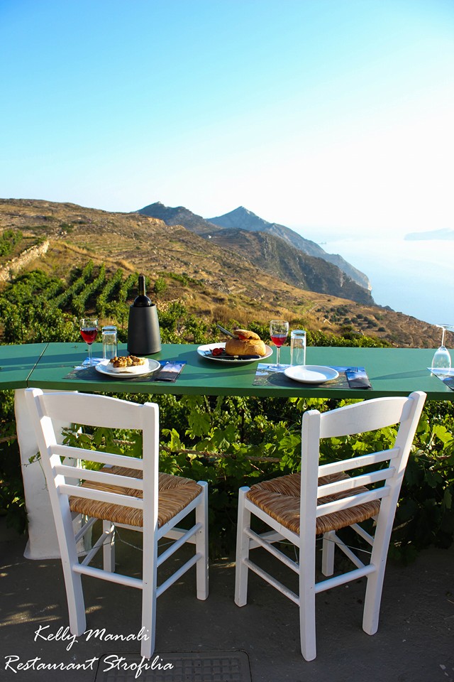 View from a balcony to the sea. A table and two chairs with food on the table and red wine. Sikinos Greece