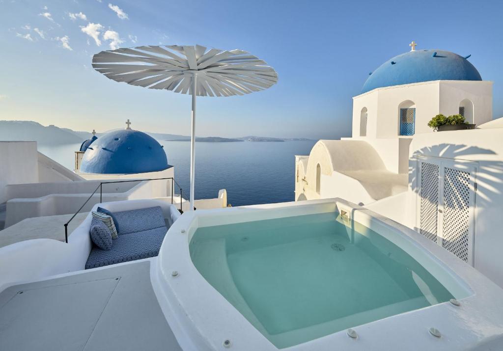 Cave Suite Oia Hotel in Santorini with a swimming pool between 2 Greek whitewashed Churches with blue dome.