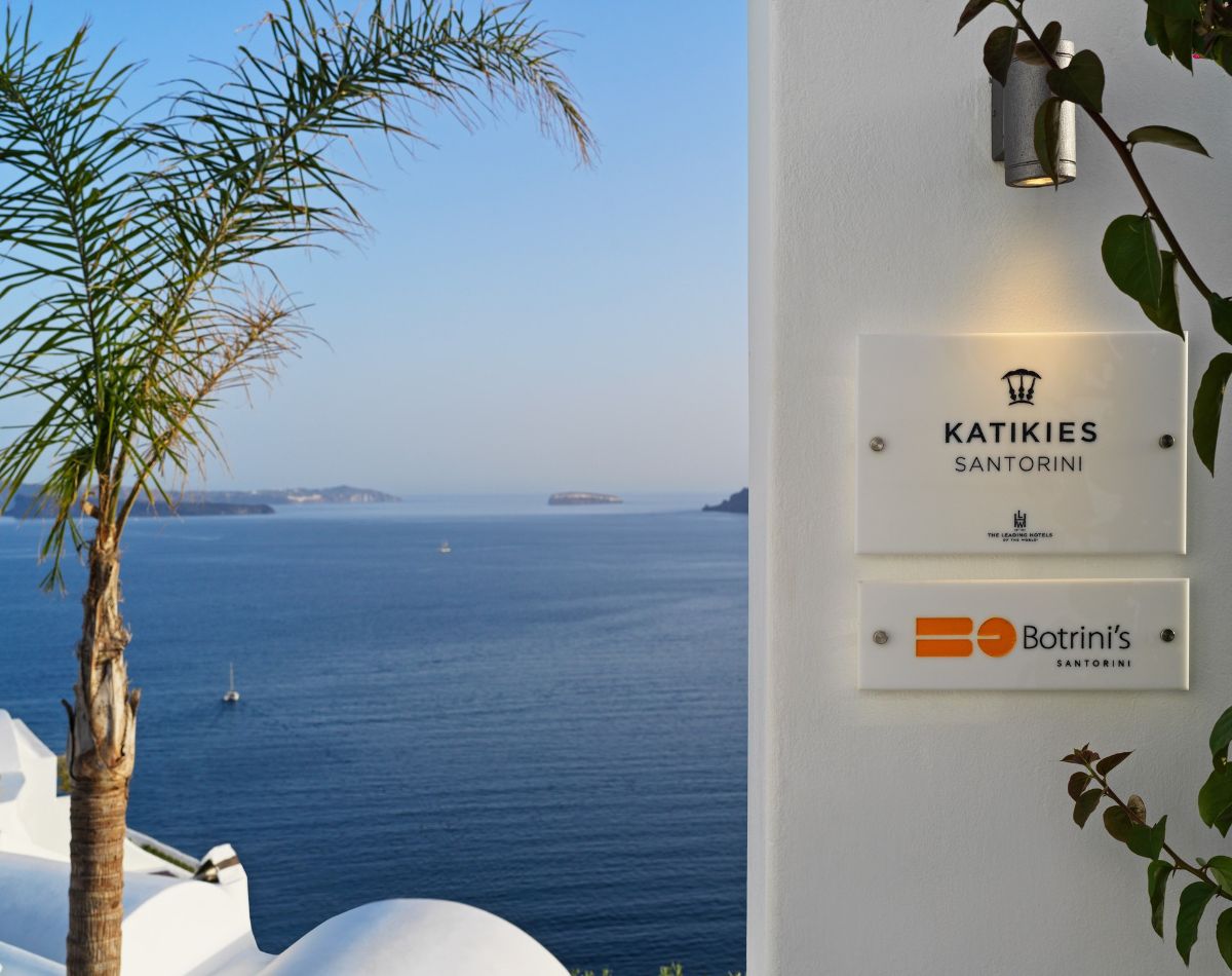 Part of the wall with signs of Katikies hotel and Botrini's restaurant in Santorini and the sea in the background.