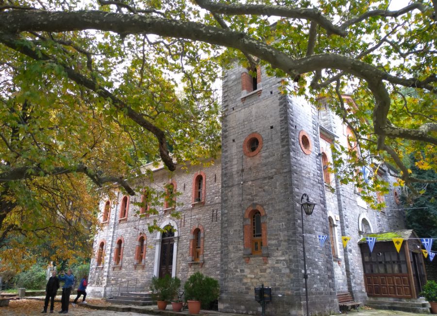 A Greek Church with many trees and three people in Tsagarada Village Pelion Greece.