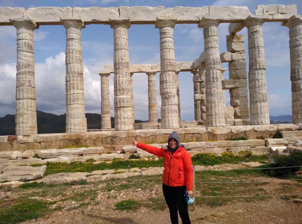 Athens Riviera. Evgenia from Travel the Greek Way pointing at the Temple of Poseidon in Cape Sounion