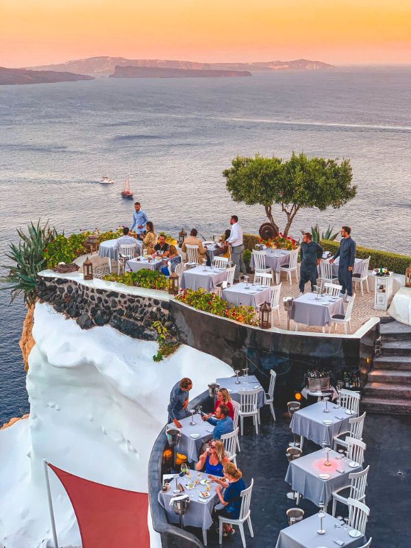 Lycabettus Restaurant with tables and chairs in the caldera with people dining. Santorini best diners.