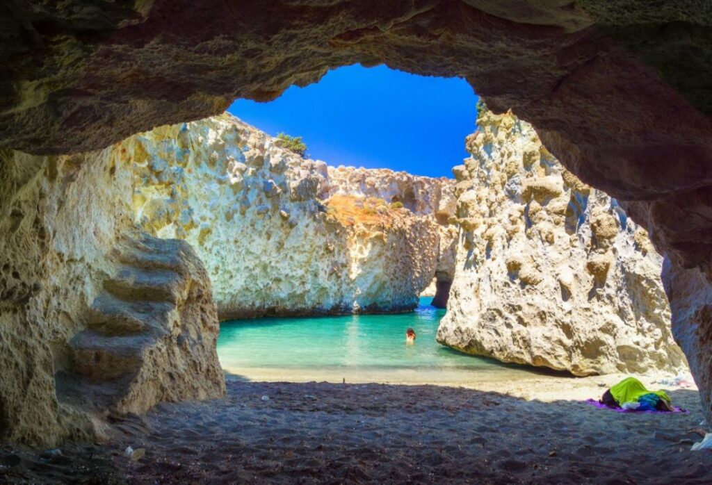 A Cave With Green Water and one Person Swimming in Milos Greece.