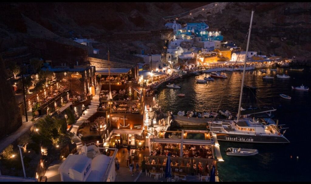 The beautiful Ammoudi Fish Tavern all lit up at night in a seafront.