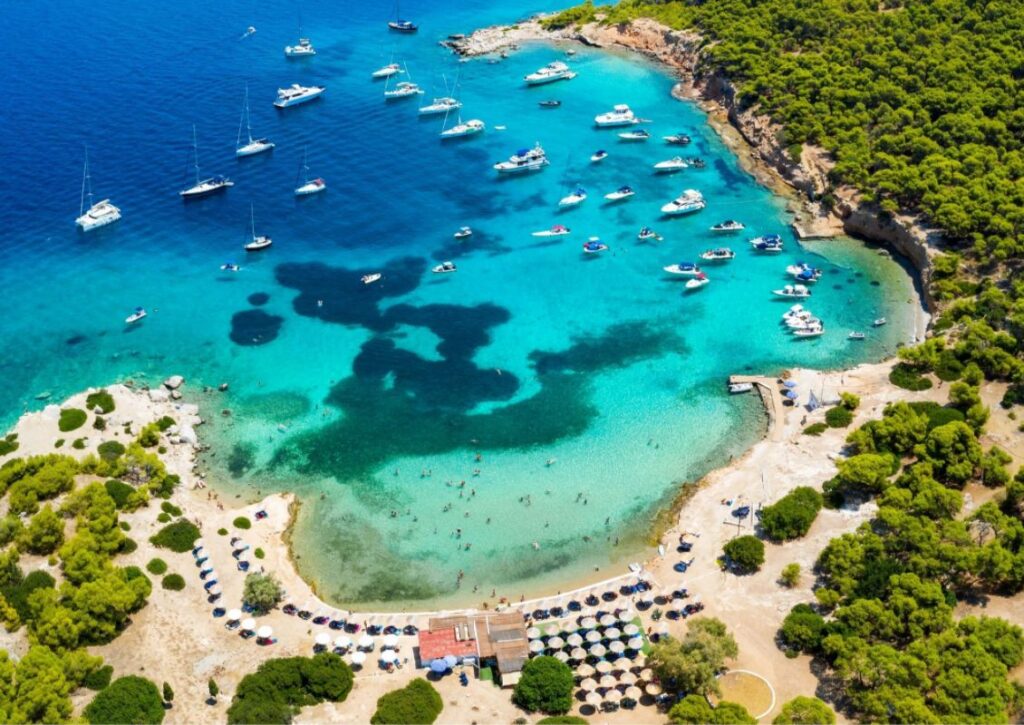 Aerial view of Moni island in Aegina with many yachts and people swimming. 