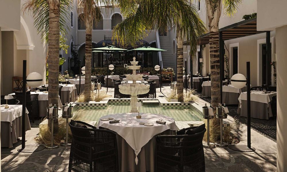 A serene courtyard dining area surrounded by palm trees and a decorative fountain in Santorini.