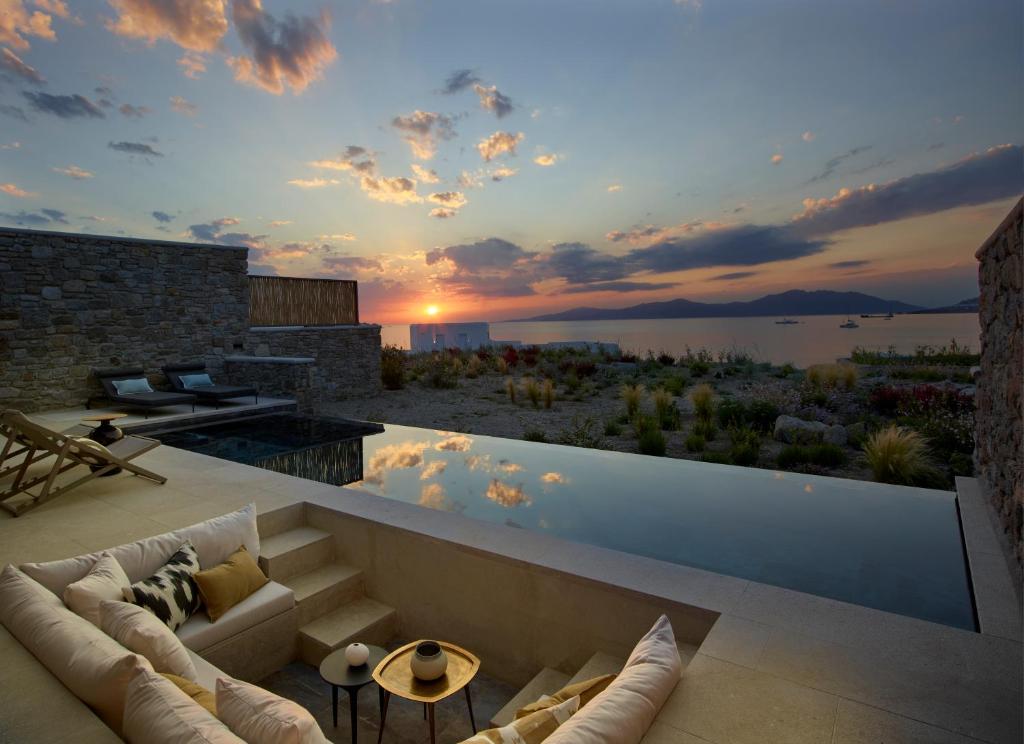 A small swimming pool and big chairs with large pillows and a view in the sea on the sun set. In Mykonos Island. 