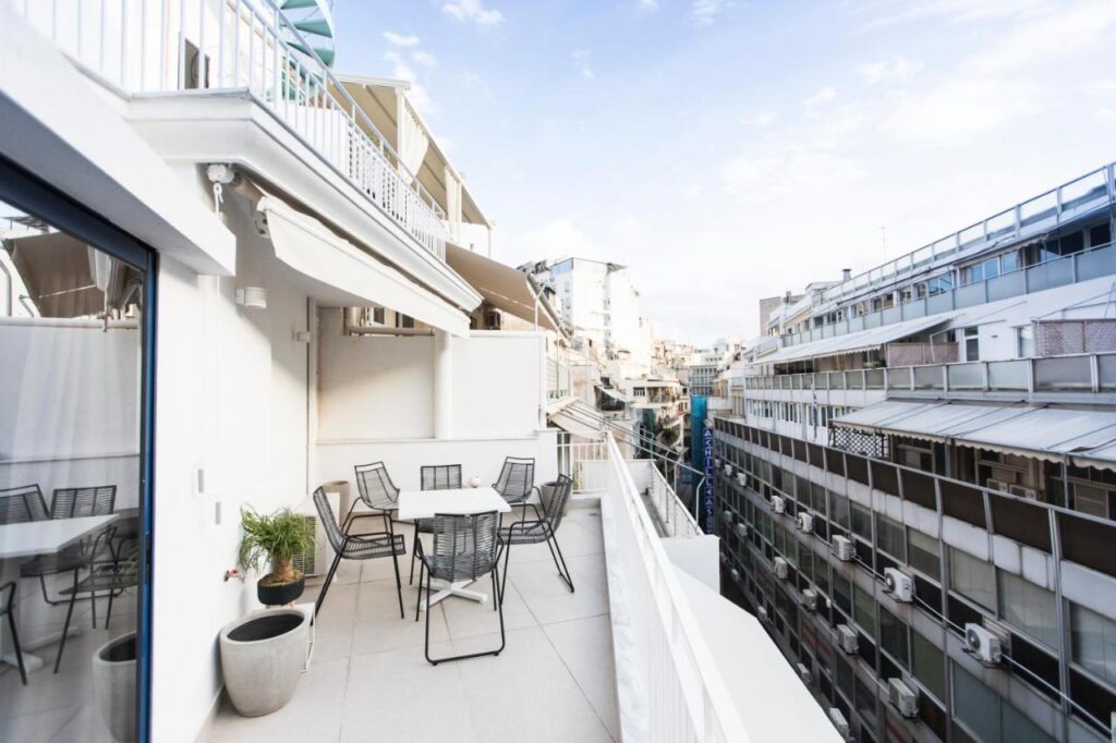 An Athens Budget Apartment  balcony with a table and six chairs and other buildings in Syntagma.