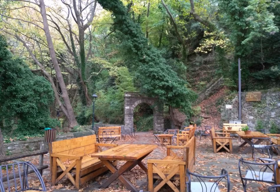 Adamenas square and Etrance to Centaurus rail, some wooden tables and chairs. The Best Things to do in Portaria.