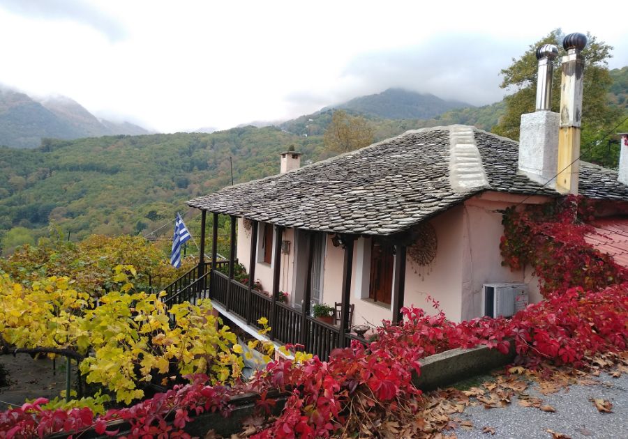 A stone-built hoouse surrounded by lush forest and orange and red leaves with a Greek flag on pelion Greece. 