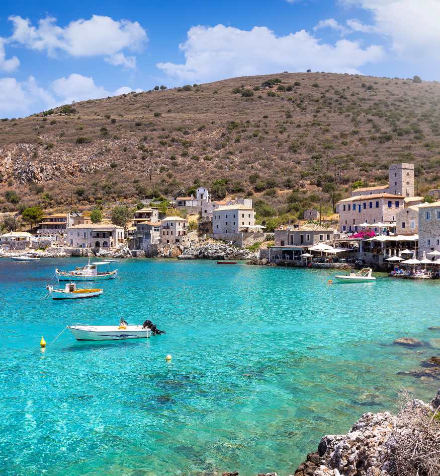 Turquoise coastal waters hitting the stone towers of the seaside village of Limeni in Mani, Greece in April.