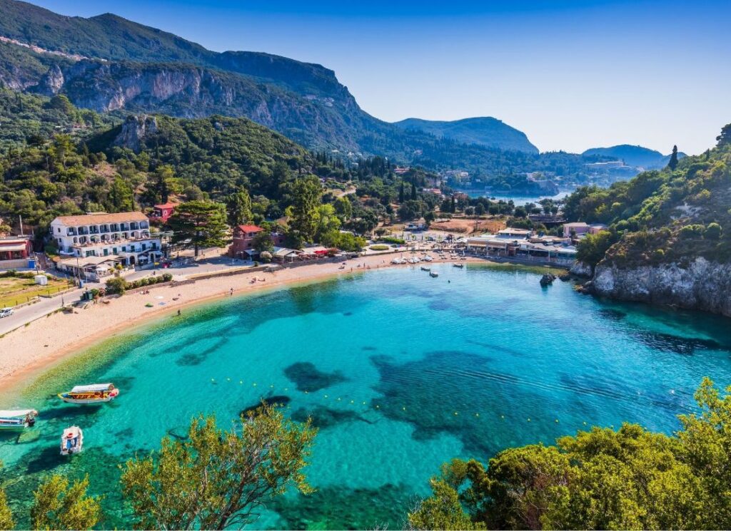  A sandy beach at Paleokastritsa Village with many people, some buildings and fish boats taken from a drone. Best things to do on Corfu island