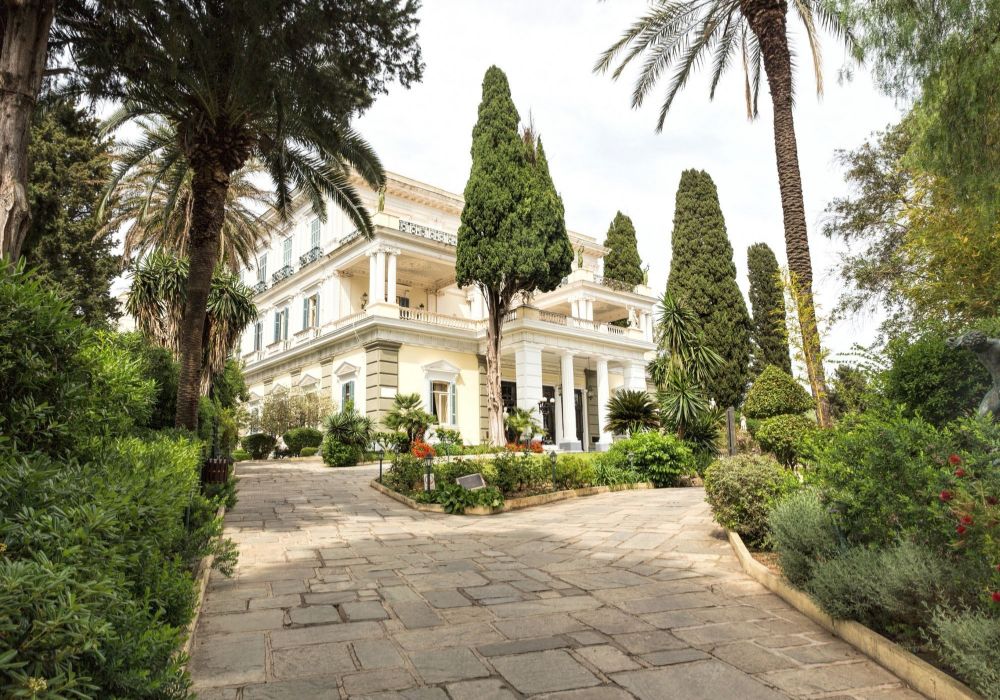 Achilleion Palace with a lot of green and trees in a sunny day. Best things to do on Corfu island.