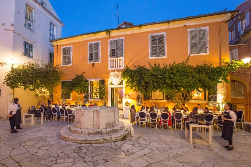 The Venetian Well with many people sitting, eating and celebrating. Best things to do on Corfu island.