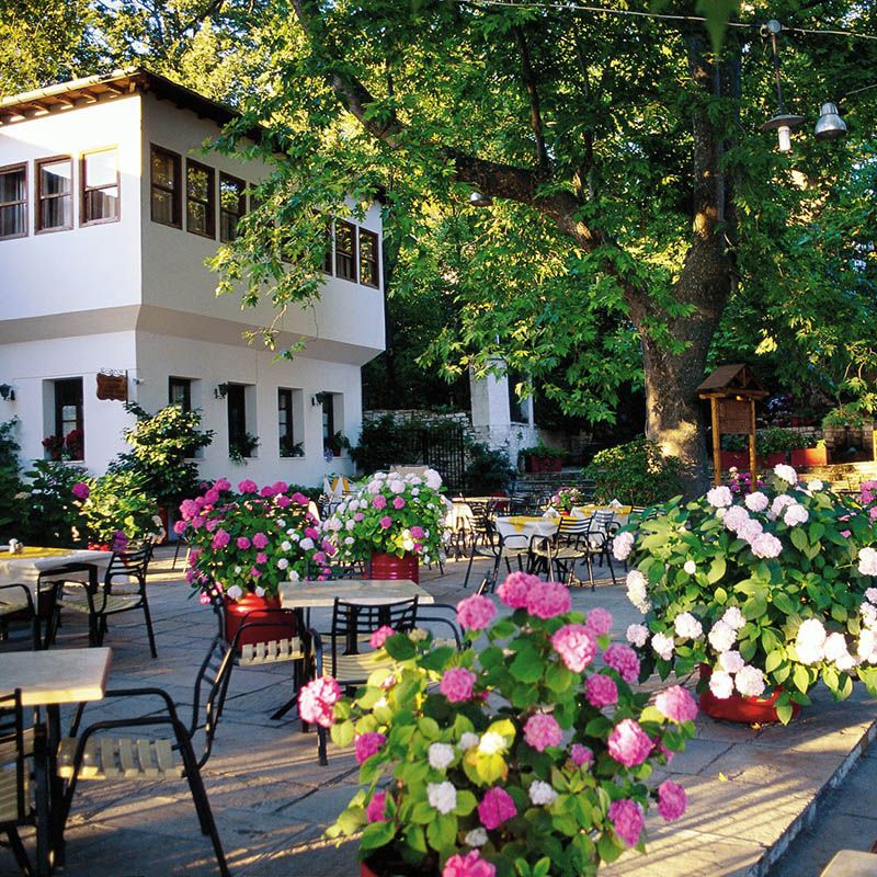 Main square in Portaria, a building, chairs and tables and many flowers in pots in Pelion Portaria.