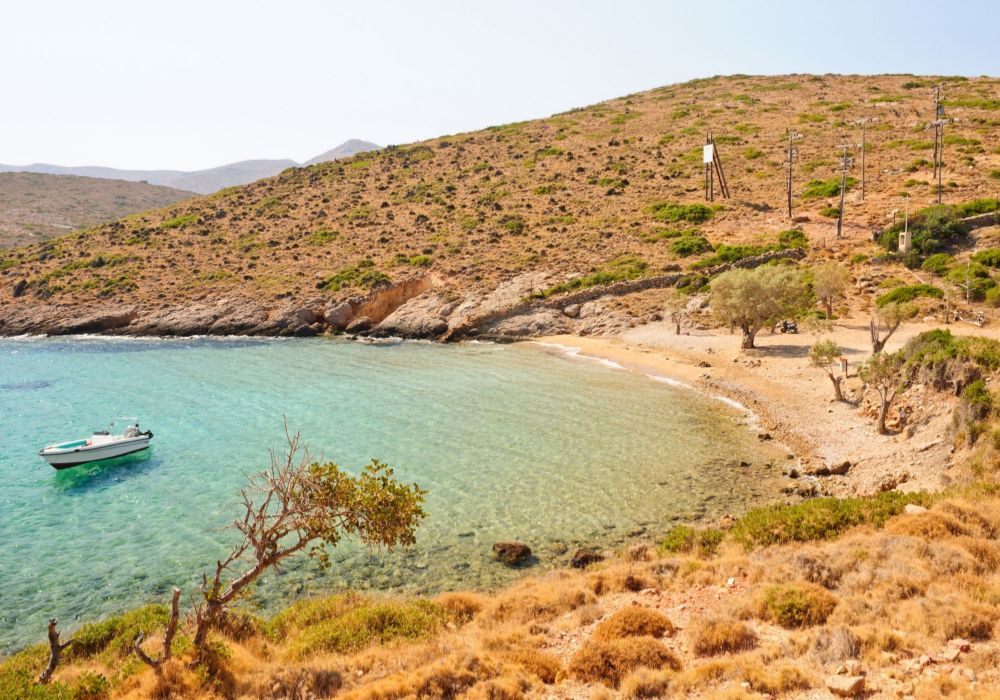 A beach in Leros Island with some olive trees and bushes and a boat in the sea in a sunny day. Off-The-Beaten-Track Greece Destinations.