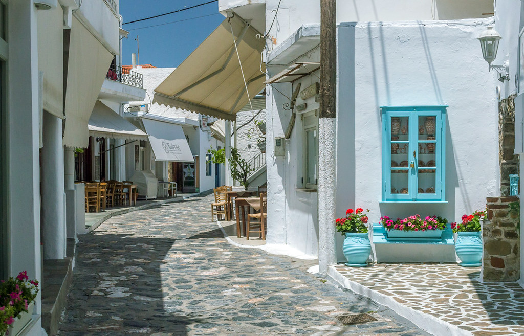 An alley with whitewashed houses and ships, some plants in pots in a sunny day.